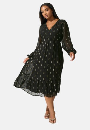 Vestido negro con estampado floral, mangas largas transparentes, escote en V, cintura fruncida y dobladillo con volantes en capas. Presenta detalles florales dorados en toda la prenda.