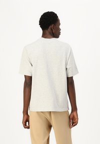 Tricou gri cu mâneci scurte, cu o croială relaxată, fabricat dintr-un material moale din bumbac. Are un guler rotund și detalii de design minime.