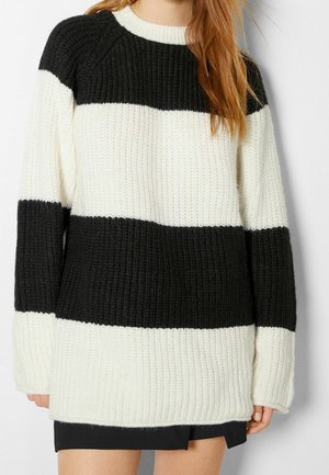 Femme portant un pull en grosse maille avec de larges rayures horizontales noires et blanches et une jupe noire.
