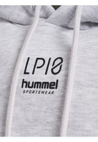 Ljusgrå hoodie med en texturerad tyg. Har svarta tryckta logotyper: "LP10" och "hummel SPORTSWEAR." Inkluderar en dragsko med ett vävt mönster.