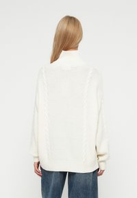 Pulover alb supradimensionat cu guler înalt, panouri texturate și detalii din tricot cablat pe umeri. Material moale, tricotat.