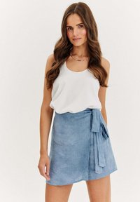 Světlé modré zavinovací sukně vyrobená z měkkého materiálu s vázačkou na straně. Kombinováno s bílým bezramínkovým topem. Hladký, ležérní design.