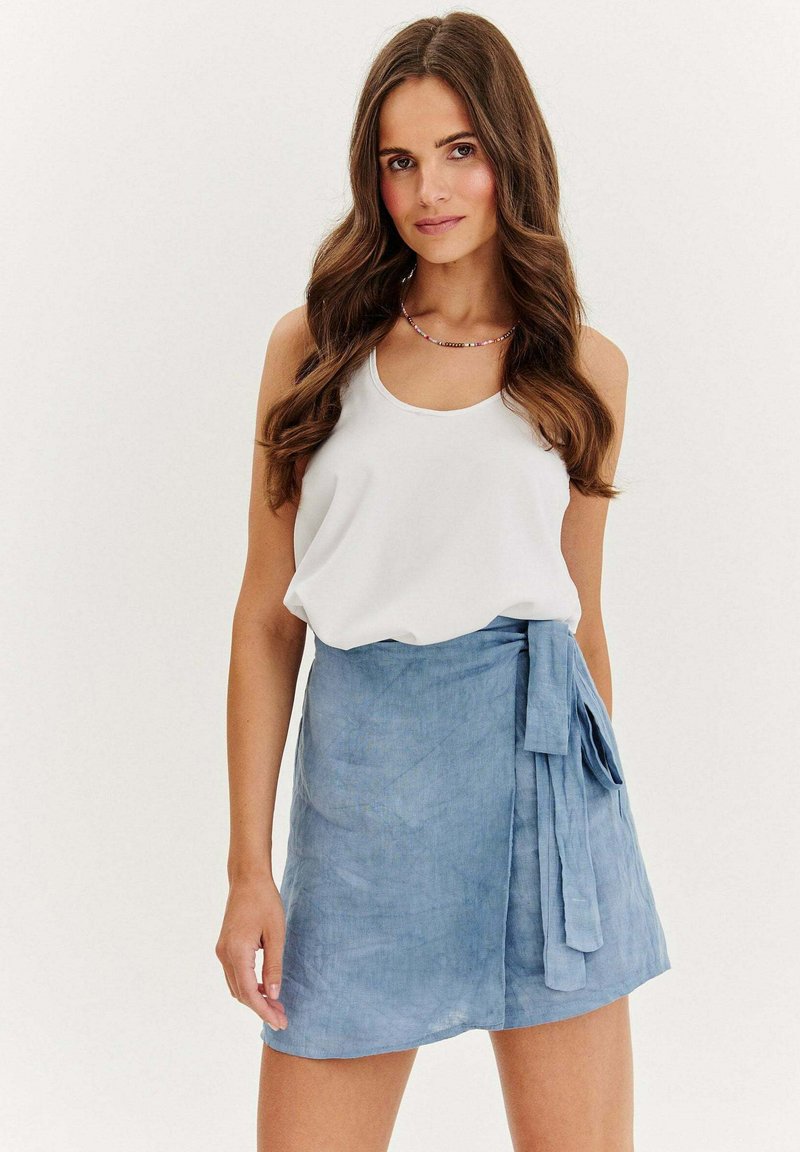 Světlé modré zavinovací sukně vyrobená z měkkého materiálu s vázačkou na straně. Kombinováno s bílým bezramínkovým topem. Hladký, ležérní design.