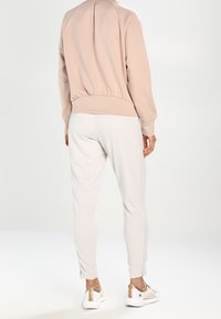 Felpa rosa chiaro con orlo e polsini a costine, abbinata a pantaloni jogger grigi chiari con strisce laterali e cerniere alle caviglie.