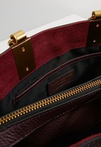 Donkerpaars leren handtas interieur met bordeauxrood suède voering. Bevat gouden hardware en ritscompartimenten voor organisatie.