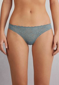 Kantstring in gedempt blauw met gegolfde randen. Heeft ingewikkelde bloem- en geometrische patronen, die een delicate, doorzichtige textuur tonen.