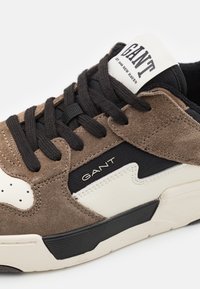 Braune Wildledersneaker mit schwarzen Akzenten. Verfügt über weiße Einsätze und ein Logo auf der Zunge. Schwarze Schnürsenkel und eine strukturierte Sohle runden das Design ab.