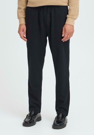 Black elastic-waist pants with a relaxed fit, featuring a smooth texture and minimal detailing. Paired with black loafers.