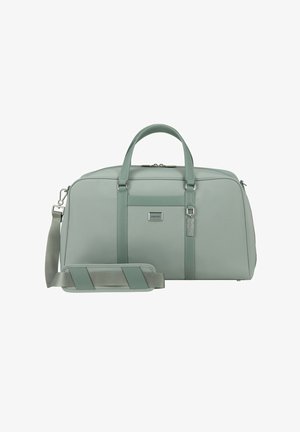 Erweiterbare Reisetasche aus weichem mintgrünem Stoff, mit zwei oberen Griffen, einem abnehmbaren Schultergurt und einem Logo-Patch auf der Vorderseite. Silbernene Akzente.