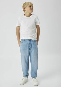 Camiseta blanca de manga corta, vaqueros de mezclilla azul claro, corte relajado y zapatillas blancas. Diseño sencillo, sin patrones ni acentos visibles.