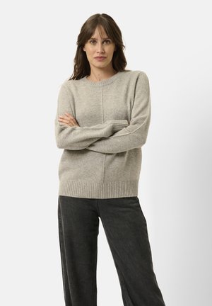 Lys grå, strikket sweater med rund halsudskæring og ribbet kant. Lange ærmer med blød tekstur, parret med mørke denim bukser med bred ben.