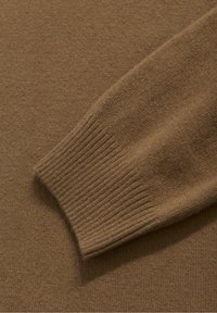 Détail d'un pull en tricot marron mettant en valeur une texture douce, un poignet côtelé et un corps lisse, soulignant l'uniformité de la couleur et la cohérence du matériau.