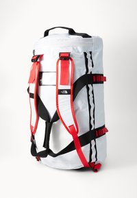 White backpack with red straps, black accents, and reflective details. Features adjustable straps and a top handle for carrying.
