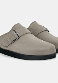 Zoccoli in suede grigi con una finitura liscia, dotati di una suola in gomma nera e una fibbia decorativa in metallo sulla cinghia per una vestibilità sicura.