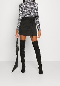 Černá semišová mini sukně s vázáním v pase, doplněná černobílým svrškem s dlouhým rukávem a vysokými černými kozačkami.