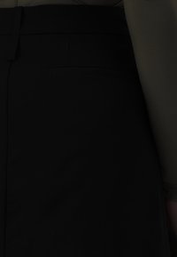 Czarne spodnie o gładkiej teksturze, z tylną kieszenią. Materiał jest usztywniony, z dopasowanym pasem i czystymi liniami.