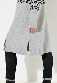 Ljust grått stickat kardigan med svart leopardmönster, ribbade ärmslut och sidofickor, kombinerat med mörka jeans och svarta ankelstövlar.