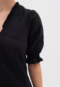 Schwarzes Leinenoberteil mit V-Ausschnitt, Rüschensaum und Puffärmeln mit elastischen Manschetten. Glatte Textur und atmungsaktiver Stoff.