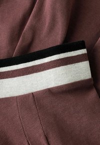 Gros plan de tissu tricoté mauve plié avec une bande de finition côtelée présentant des rayures horizontales noires, blanches et mauves.