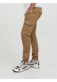 Beige Cargo-Hosen im entspannten Schnitt mit mehreren Taschen, elastischen Bündchen und einer glatten Baumwollmischung, kombiniert mit sportlichen weißen Turnschuhen.