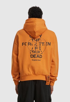 Orange hoodie with a large black graphic text on the back, featuring a circular design and additional branding label on the side hem.