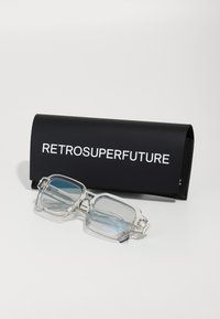 Ochelari dreptunghiulari clare cu lentile de un albastru deschis, așezați pe un toc negru cu text alb „RETROSUPERFUTURE.” Material neted și design modern.