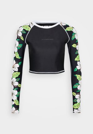 Svart cropped langermet topp med hvite blomster mønster på ermene, hvit kragekant og "IT'S NOW COOL" tekst på brystet.