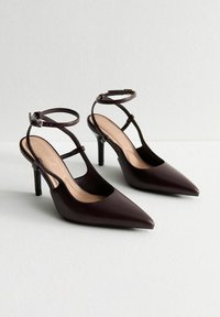 Scarpe con tacco a punta in pelle marrone scuro, caratterizzate da due cinghie alla caviglia con fibbie e lati aperti per una migliore traspirabilità.