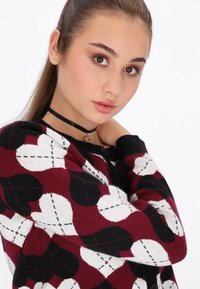 Maglione rosso e nero con motivo a cerchi bianchi e neri, dotato di colletto rotondo e bottoni lungo la parte anteriore.
