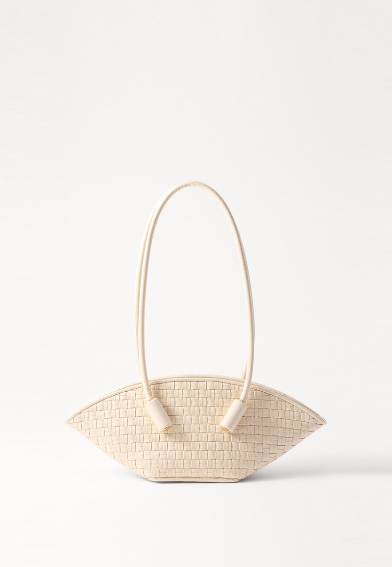 Vävd beige handväska med en unik böjd form, med två texturerade handtag och cylindriska metallaccent.