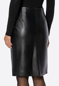 Czarna skórzana ołówkowa spódnica o gładkiej fakturze, z rozcięciem z tyłu i detalem na szwie bocznym, wokół której stylizowano dopasowany czarny top.