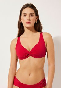 Röd bikiniöverdel med en tvinnad tygdetalj i mitten, breda remmar och mjuk textur. Lämplig för badkläder.