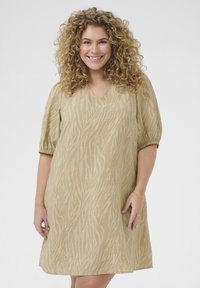 Vestido beige de manga corta con escote en V y tejido texturizado que presenta un sutil patrón de cebra. El diseño es holgado y llega a la rodilla.