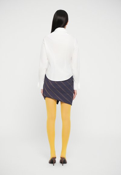 Wit overhemd met kraag, marineblauwe rok met diagonale strepen, gele maillot en bruine hakken. Achteraanzicht met een eenvoudige witte achtergrond.