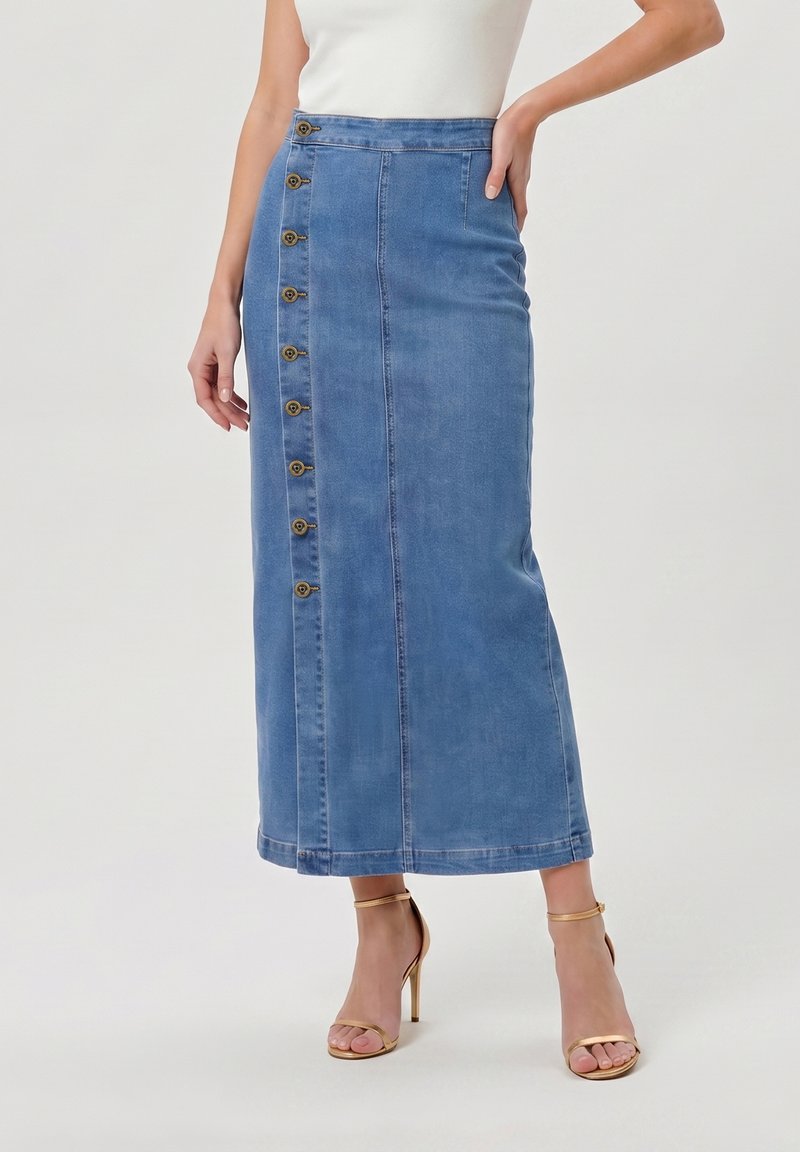 Femme portant une jupe midi en denim bleu taille haute avec des boutons sur le côté et des sandales à talons hauts à bride cheville dorées.