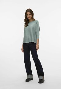 Un pull vert clair à coupe ample et texture côtelée, assorti à un jean en denim foncé avec des ourlets retroussés et des chaussures noires.