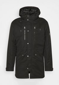 Svart parkajacka med huva, utrustad med fickor med dragkedja, tryckknappar och justerbara dragsnören. Slätt, slitstarkt tyg, midilängd design.