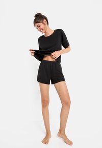 Svart t-shirt med kort ärm och elastisk nederkant, kombinerad med svarta shorts som har dragsko i midjan och tre knappslut.