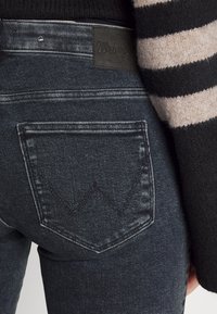 Mörk denimjeans med en formad bakficka som har en kontrasterande söm. Vävlabel på midjan, i kombination med en randig stickad tröja.