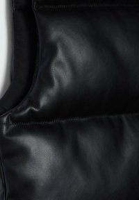 Černá kožená vesta s hladkým povrchem, se zpevněným designem a viditelným švem podél okrajů. Bez kovových prvků nebo vzorů.