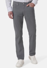 Graue Jeans mit geradem Bein, Fronttaschen und Knopfverschluss. Kombiniert mit weißen Turnschuhen und einem gemusterten Hemd.