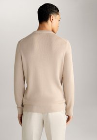 Maglione lavorato a maglia beige chiaro con maniche lunghe, polsini a coste e un motivo testurizzato. La vista posteriore mostra un collo rotondo semplice.