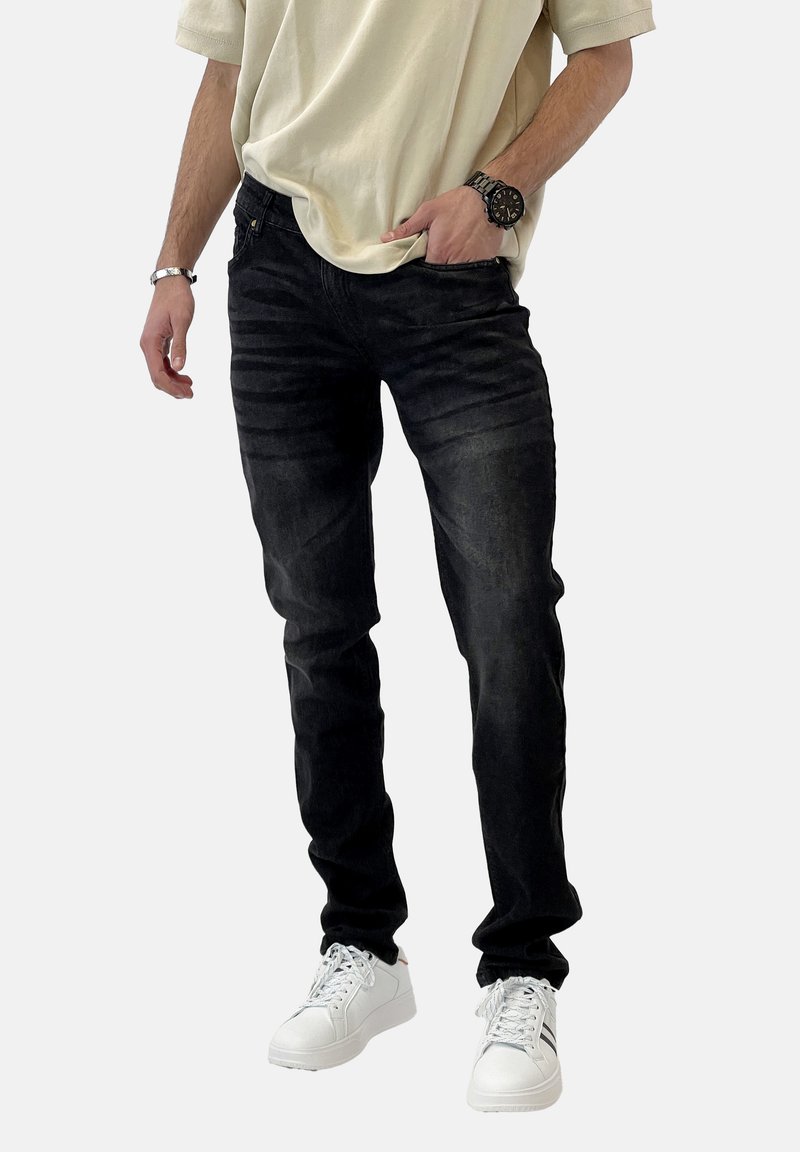 Vaqueros de mezclilla negros con corte ajustado, que presentan un ligero desgaste y un diseño clásico de cinco bolsillos, combinados con zapatillas blancas.