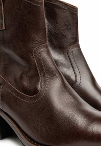 Brown leather ankle boots with a smooth texture, elastic side panels, and a low stacked heel. Stitching detail is visible around the seams.
