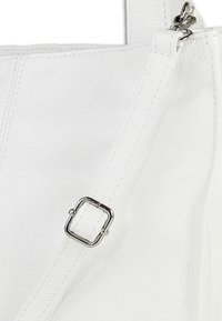 Detail van een witte leren handtas met een gestructureerd oppervlak, contrasterende witte stiksels en een zilverkleurige metalen gesp op de verstelbare riem.