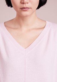 Sweter z dekoltem w serek w miękkim różowym dżerseju z prążkowanymi brzegami, z centralnym szwem i luźnym krojem wokół szyi i ramion.