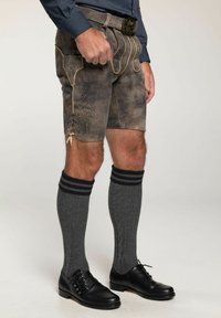 Bruine leren shorts met decoratieve stiksels, veters aan de zijkant, gecombineerd met grijze kniekousen en zwarte nette schoenen.