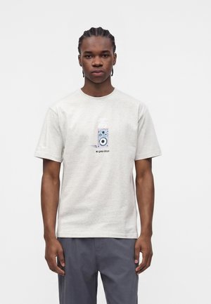 Ung mand med cornrows iført en lysegrå T-shirt med et grafisk højttalerdesign og teksten "grey days", kombineret med mørkegrå bukser.