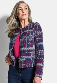 Strickjacke mit einem mehrfarbigen Karomuster in Blau, Rot und Grau. Verziert mit zwei dunklen Knöpfen und einem verkürzten Schnitt. Weicher Stoff.