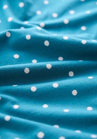 Turkos tyg med vita prickar, mjuk textur och lätt drapering, som visar ett enhetligt mönster över ytan.